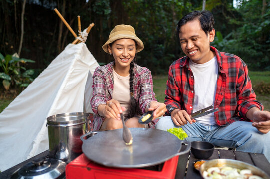 Indonesian southeast asian couple preparing for an outdoor meal, showcasing a portable stove and various ingredients. The scene of the lifestyle of enjoying food in a natural setting