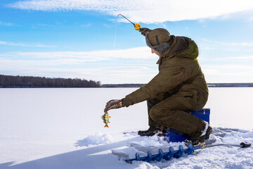 Fishman ice fishing on frozen lake at sunny winter day.