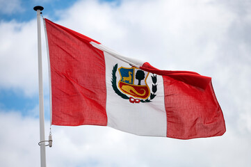 Peru flag fluttering in the wind with a blue sky and cloud background. 