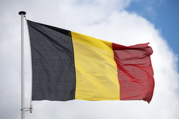 Belgium flag fluttering in the wind with a blue sky and cloud background. 
