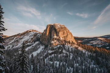 A stunning winter rock structure blanketed in snow, illuminated by the soft light of dawn, with evergreen trees enhancing the peaceful scene.