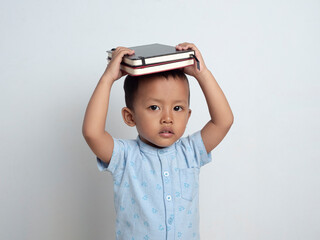 Happy cute and cheerful Asian boy holding a book above his head on an isolated white background....