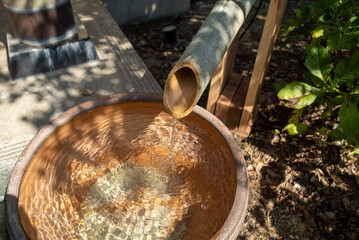 Traditional bamboo spout pouring water into basin in Japanese garden