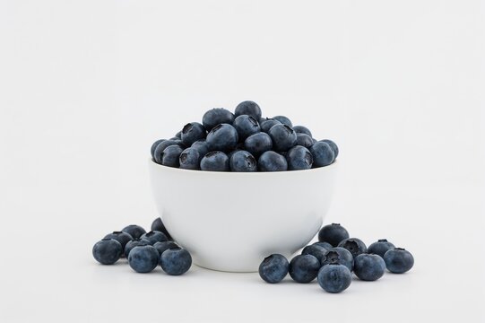 White bowl filled with fresh blueberries on a plain white surface, ample space for text