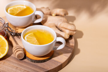 Cups of hot tea with ginger, honey and lemon on light background