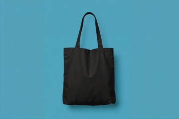 Eco-friendly black fabric tote bag mockup for women's shoulder, isolated on a blue backdrop (clipping path)