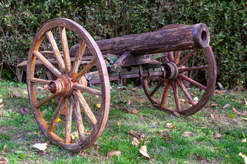 Fototapeta premium Rustic antique wooden cannon with large wheels. A historical weapon displayed in a garden on green grass