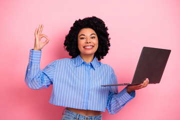 Confident young woman holding a laptop and showing an OK hand gesture against a vibrant pink background