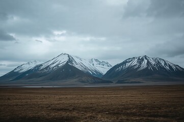 Fototapeta premium Breathtaking view of rugged, snow-topped peaks amidst expansive moorlands beneath an overcast sky.