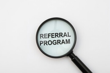 Business idea. The phrase REFERRAL PROGRAM seen through a magnifying glass on an open business book, overhead shot, conceptual image