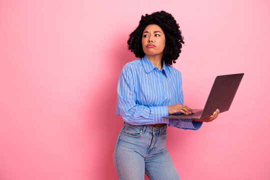 Young woman with laptop on pink background in casual fashion, showcasing trendy style and curious expression