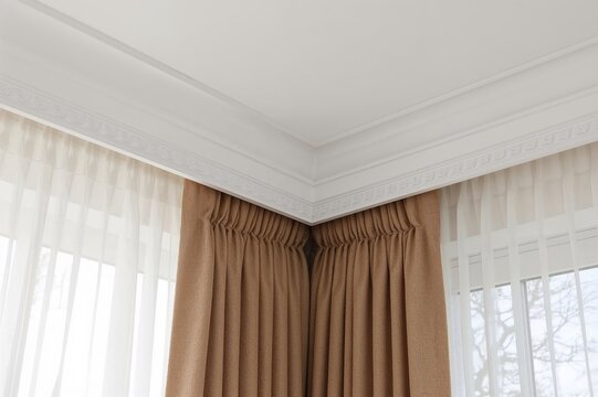 Close-up of interior showing white ceiling with plastic cornice featuring double rails and layered curtains including brown matting and sheer fabric