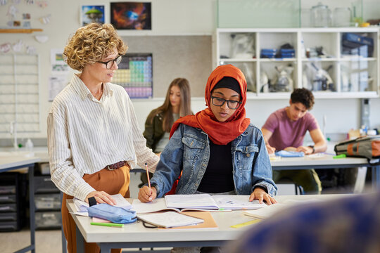 Teacher helping  female student with hijab during lesson - Powered by Adobe