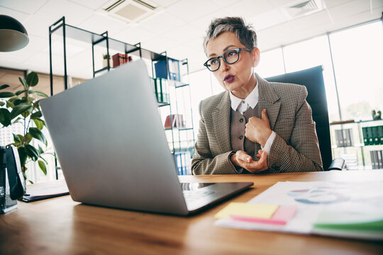Senior professional speaking during an online meeting in a modern office setting with contemporary decor and natural light