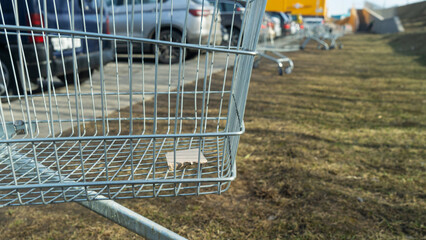 Shopping cart closeup on grass near parked cars outside retail store. Retail logistics and consumer...