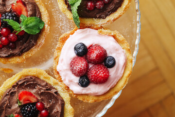Sweet mini tartlets with cream and berries. Dessert with chocolate mousse and fruit topping. Homemade pastry with blueberries strawberries and raspberries. Fresh sweet cakes served on glass plate.