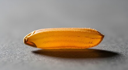 Close-up of a single grain of raw golden rice, highlighting its texture and amber color against a dark background