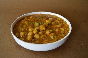Authentic chole masala curry served in a bowl on a brown background. Traditional Indian dish made with chickpeas simmered in onions, tomatoes, and aromatic spices.