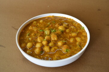 Authentic chole masala curry served in a bowl on a brown background. Traditional Indian dish made with chickpeas simmered in onions, tomatoes, and aromatic spices.