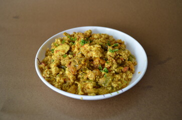 Delicious paneer bhurji served in a bowl on a brown background. A traditional Indian vegetarian dish made with scrambled cottage cheese, onions, tomatoes, and spices.