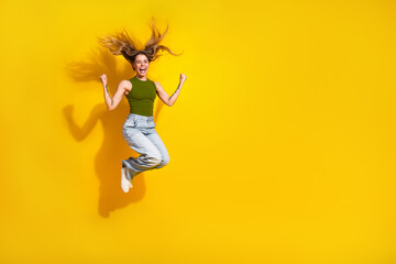 Obraz premium Cheerful young woman jumping high on a vibrant yellow background showing excitement and happiness in casual khaki attire