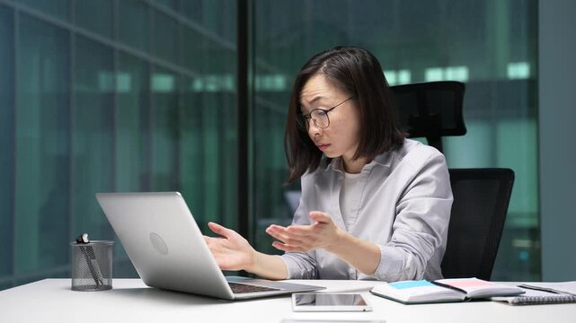 Frustrated asian businesswoman complains about poor performance of software on laptop sitting in business office. Confused female employee is dissatisfied with work of computer, internet or service