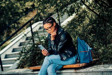 Fototapeta premium Young woman in casual leather jacket outdoors using her smartphone, enjoying lifestyle and natural surroundings on a sunny day