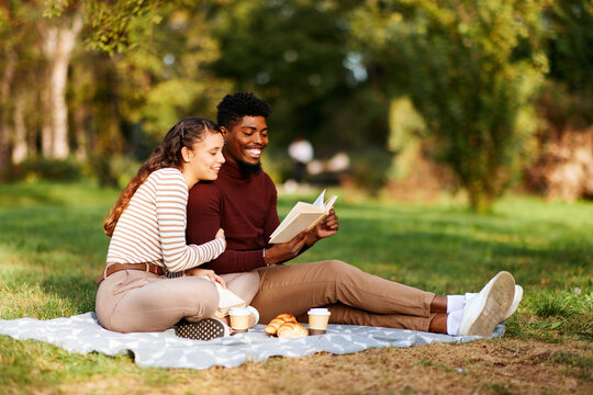 Happy multi-ethnic couple enjoying a book and picnic in autumn park
