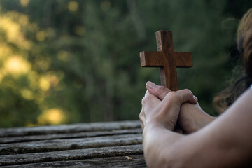 A wooden cross in the  hands of a person praying in the nature.