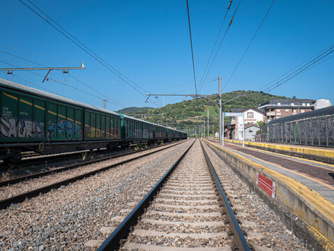 Toral de los Vados, Leon, Spain, 06-16-2025: Main track of the station between the passenger building and some parked cars and a high signal in the background with the red light on indicating a stop