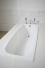 Modern white bathtub with chrome faucet and shower head in bathroom interior
