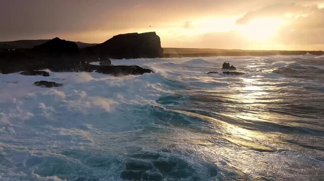 Dramatic aerial view of rough ocean waves crashing a sunset.