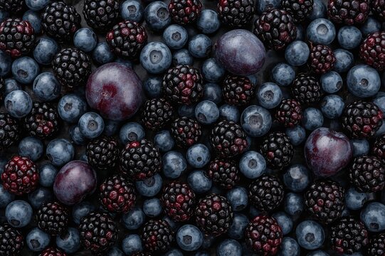 Assortment of dark blue and black fruits on a fresh background. Overhead shot featuring ripe berries, plums, and grapes.
