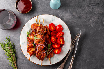 Pork kebab with barbecue sauce and tomatoes and a glass of red wine on a grey background top view