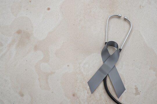 Grey ribbon and stethoscope placed on a concrete surface representing awareness for neurological diseases such as Parkinson's and brain cancer - Powered by Adobe