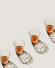 Transparent alcohol Glasses at line with shadow at sunlight on beige concrete table, top view minimal style, aesthetic pattern shiny glass sparkling at natural light, summer strong drink