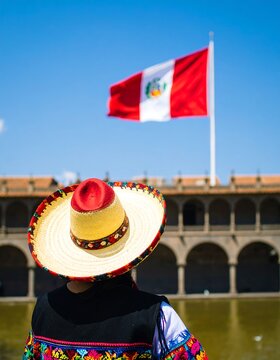 Person wearing a hat and traditional clothing, looking at a Peruvian flag