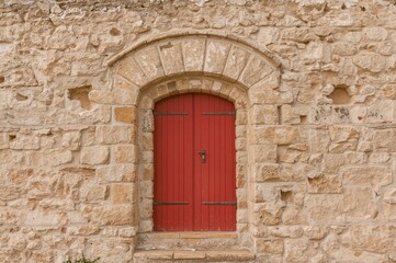 A vertical photo featuring a weathered brick wall with an arched entrance and a crimson door