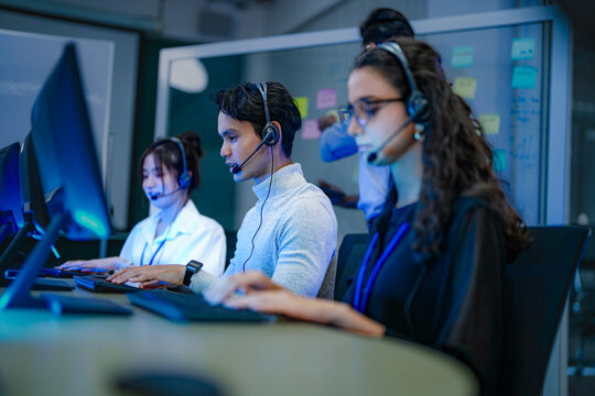 A diverse team of customer service agents wearing headsets works in a modern call center. Professional operators provide technical support and assistance to clients day and night. - Powered by Adobe