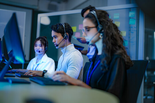 A diverse team of customer service agents wearing headsets works in a modern call center. Professional operators provide technical support and assistance to clients day and night. - Powered by Adobe