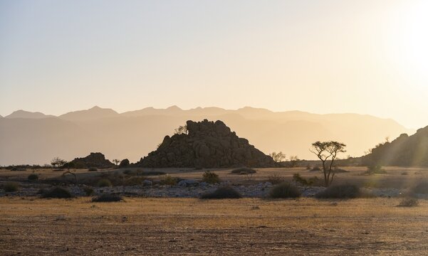 Desert landscape in the evening light at sunset, barren landscape with hills of stacked rocks, backlit, Brandberg in the background, Erongo, Damaraland, Namibia
