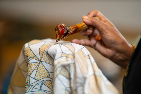 Close-up of an artisan applying hot wax with a canting on patterned fabric—traditional batik making for textile design, craft tutorials, heritage and culture visuals.