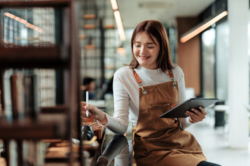 Young asian female barista using digital tablet and stylus pen for managing inventory in coffee shop