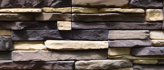 Textured stone wall featuring a blend of gray and beige stones arranged in an alternating pattern, creating a rustic atmosphere ideal for various architectural styles