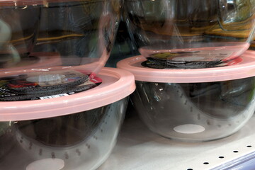 Clear plastic mixing bowls with pink lids displayed on a store shelf in a kitchen supplies section during daytime shopping hours