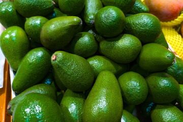 Fresh green avocados piled together at a bustling market during midday in a vibrant outdoor setting