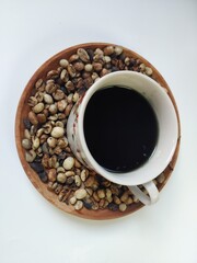 A cup of coffee inside the coffee beans on a wooden plate. Flat lay composition on a white background.