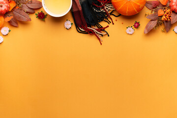 Cozy autumn flat lay composition with woolen scarf, cup of herbal tea and bright decorations on light terracotta background with copy space for your design.