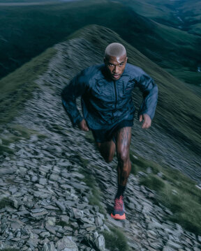 An African American male runner is running over rocky terrain with a blurred focus. Intense outdoor training.