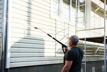 Cleaning the vinyl siding wall with a high-pressure washer.